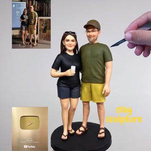 May include: A clay sculpture of a couple, dressed in casual attire, standing on a black base. The woman wears a black shirt and shorts, while the man wears a green shirt and yellow shorts. A gold YouTube play button is in the image.