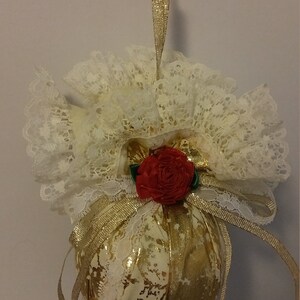 May include: A gold and white Christmas ornament with a red rose and white lace trim.
