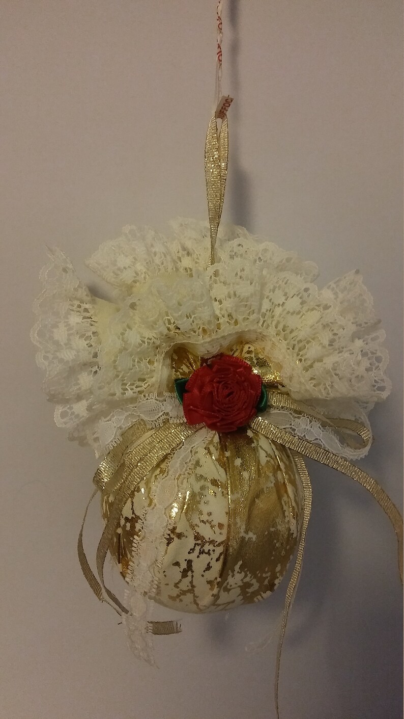 May include: A gold and white Christmas ornament with a red rose and white lace trim.