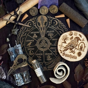 May include: A collection of ritual items including a circular black wooden board with engraved text and symbols, a round wooden slice with a raven and the word Samhain, two grey candles with skull accents, a glass vial of black salt, and metal coins.