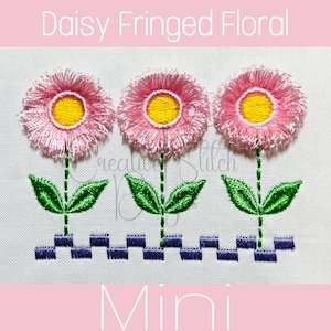 May include: Three pink daisy flowers with yellow centers and fringed petals, each with green leaves and a stem. The flowers are arranged in a row with a blue and white checkered border at the bottom. The text "Daisy Fringed Floral Mini" is at the top of the image.