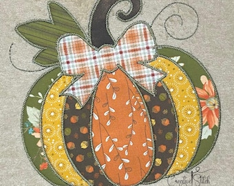 Puede incluir: Un aplique decorativo de calabaza con un lazo a cuadros, hojas y tallo. La calabaza está compuesta por varias telas estampadas en tonos naranja, amarillo, verde y marrón. El diseño está delineado con una puntada gris oscuro. El texto "Creative Stitch Designs" es visible.