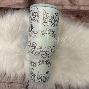 A turquoise tumbler with a floral design on it, placed on a white furry surface.
