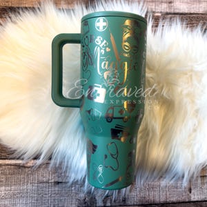 May include: A teal insulated tumbler with a handle, featuring gold and silver engraved medical-themed designs. The tumbler includes the name "Maggie" and the words "Nurse Life." The tumbler is decorated with medical symbols and the words "Engraved Expression Co."