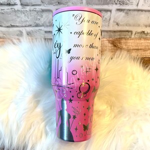 A pink and white tumbler with a quote printed on it, sitting on a white fur surface.