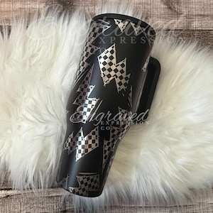 A black and white checkered patterned tumbler mug is placed on a white furry surface.