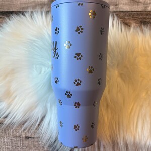 A blue tumbler with paw prints printed on it, placed on a white furry surface.