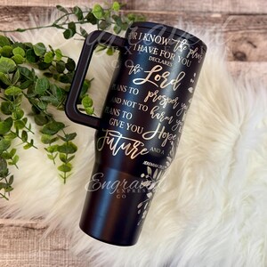 A black insulated tumbler mug with text printed on it, placed on a white fur rug.