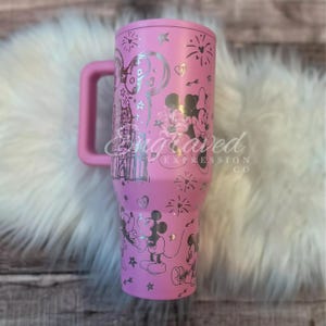 A pink tumbler mug with a handle and various Disney-themed designs, including Minnie Mouse and Mickey Mouse, printed on it.