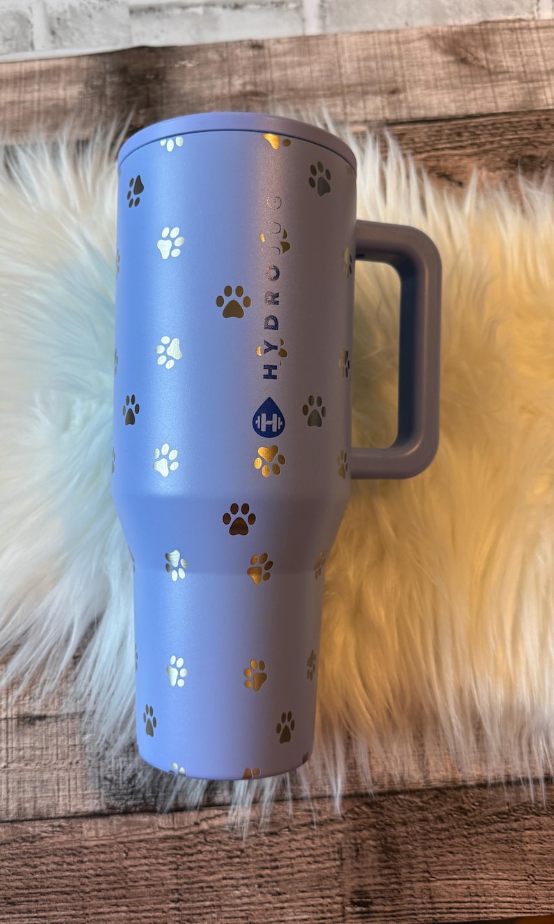 A blue insulated travel mug with paw prints printed on it, placed on a white fur rug.