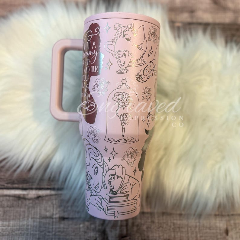 Puede incluir: Un vaso de color rosa claro con asa, con ilustraciones plateadas de personajes y elementos de un cuento de hadas. El dise&ntilde;o incluye una rosa en una campana de cristal, personajes y texto. El vaso tiene un asa grande.