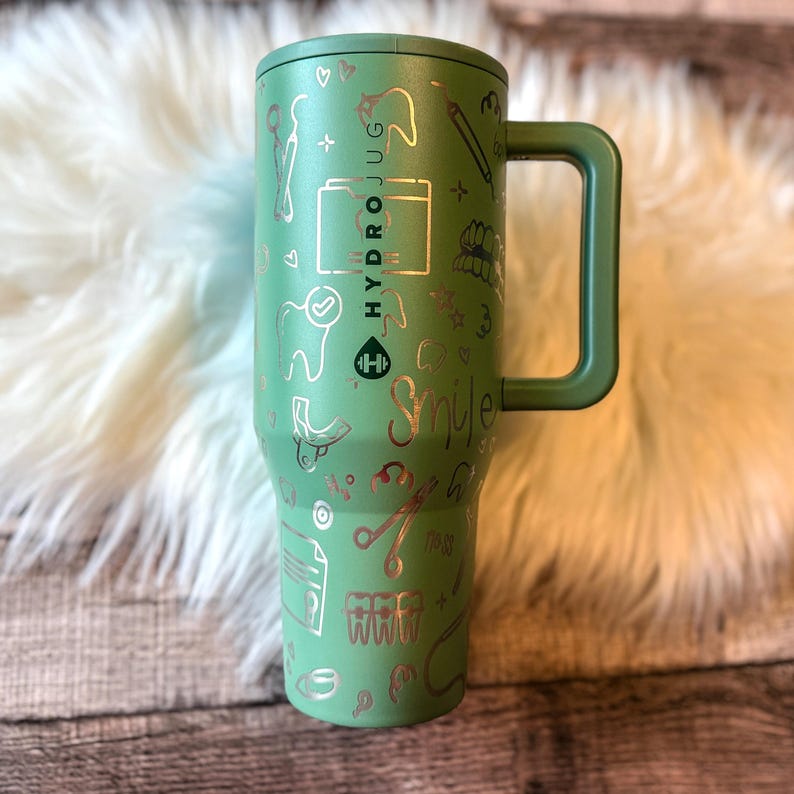 A green thermos mug with various dental-related icons and text printed on it, placed on a white fur surface.