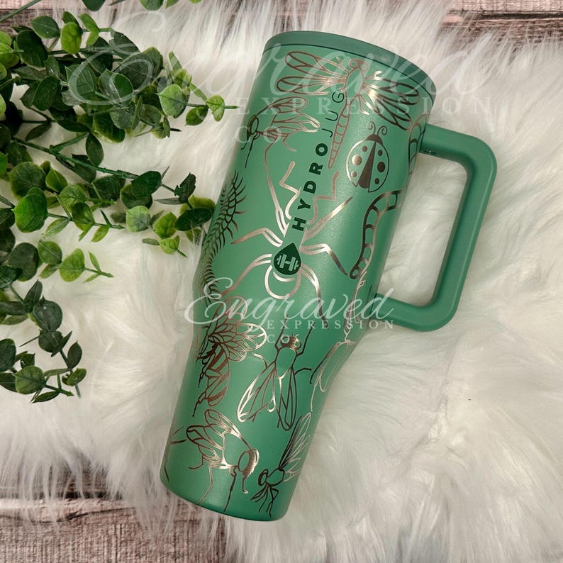 以下が含まれることがあります： 緑色のHydro Jug（ハイドロジャグ）で、ハンドル付き。より明るい緑色で昆虫のデザインが刻まれています。「Hydro Jug」と「Engraved Expression」の文字が入っています。トンボ、ハチ、クモなどの昆虫のデザインが含まれています。