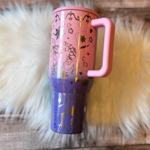 A pink and purple tumbler mug with a handle, featuring a design of characters from the Disney film Tangled.