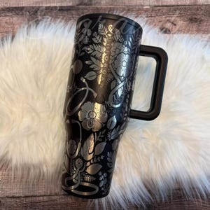 A black and silver insulated tumbler mug with a handle, placed on a white furry surface.