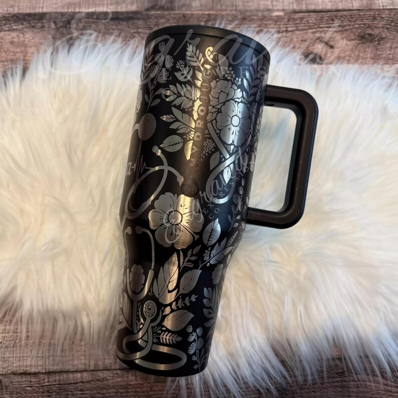 A black and silver insulated tumbler mug with a handle, placed on a white furry surface.