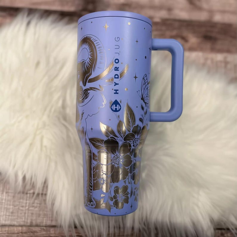 A purple stainless steel travel mug with a floral design and the text "HYDRO JUG" printed on it, placed on a white fur rug.