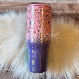A pink and purple tumbler with a Disney princess design, featuring a princess and a unicorn, is shown against a white fur background.