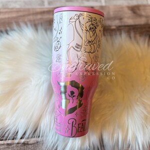 A pink and white tumbler with a Disney-themed design, featuring characters from the Disney film Beauty and the Beast.