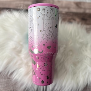 A pink and white tumbler mug with a cartoon character design, featuring a smiling character and various other cartoon-style elements.