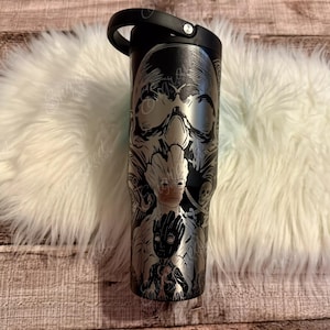 A black tumbler mug with a skull design and a handle, placed on a white furry surface.