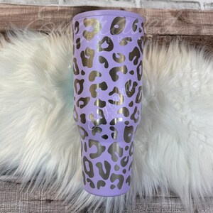 A purple leopard print tumbler sits on a white furry surface.