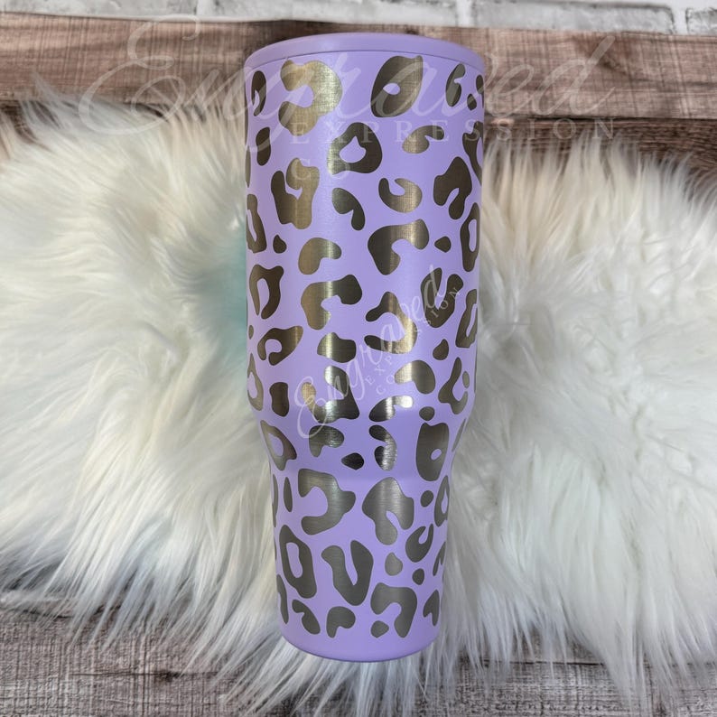 A purple leopard print tumbler sits on a white furry surface.