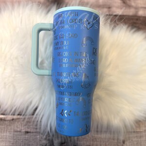 A blue tumbler mug with various Bible verse references and illustrations printed on it, placed on a white fur surface.