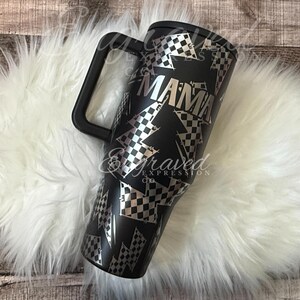 A black and white patterned tumbler mug with a handle, placed on a white furry surface.