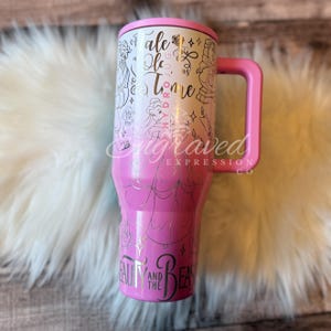A pink and white tumbler mug with the text "Beauty and the Beast" printed on it, sitting on a white fur surface.