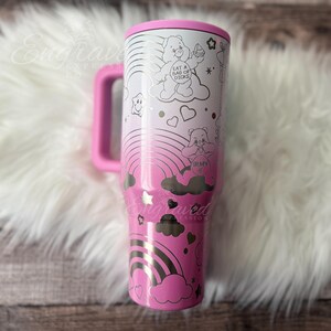 A pink and white tumbler mug with a whimsical design featuring a pink bear, clouds, rainbows, and stars.