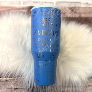 A blue tumbler with text and illustrations printed on it, placed on a white fur surface.
