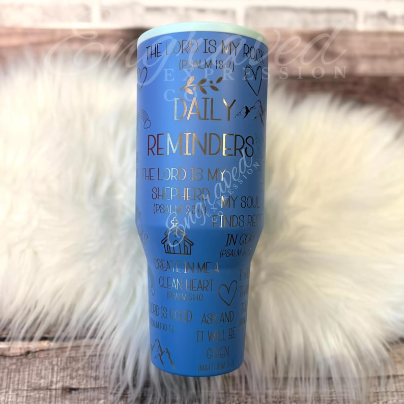 A blue tumbler with text and illustrations printed on it, placed on a white fur surface.