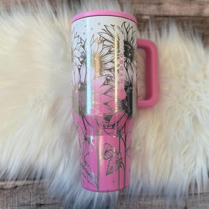 A pink and white stainless steel tumbler mug with a floral design, placed on a white furry surface.