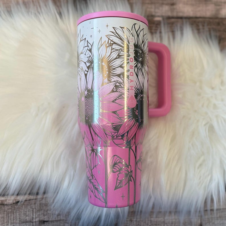 A pink and white stainless steel tumbler mug with a floral design, placed on a white furry surface.