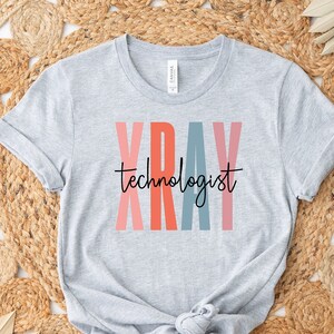 May include: Gray t-shirt with the text "XRAY technologist" in colorful letters. The letters are in shades of pink, orange, blue, and red.