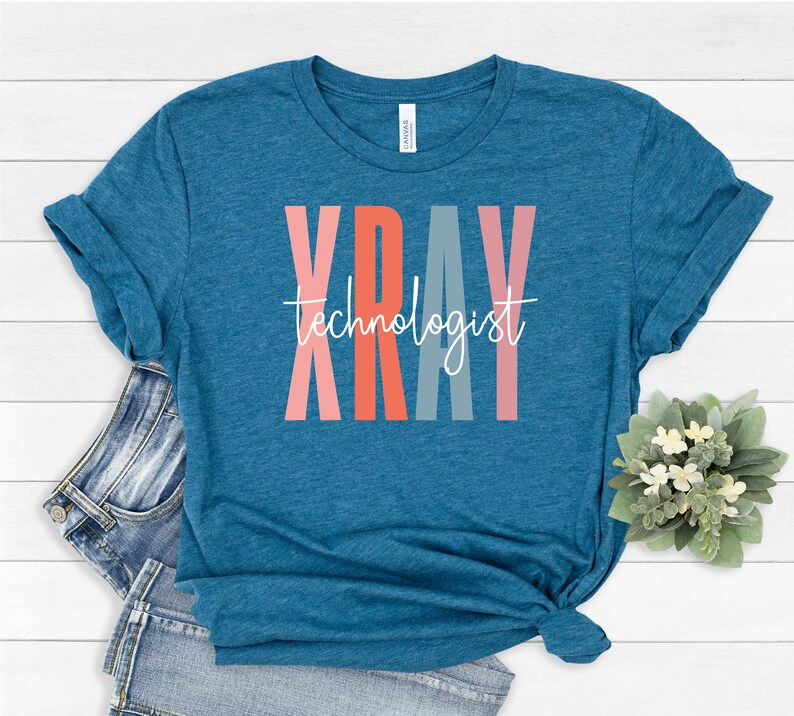 May include: Teal blue t-shirt with the word "XRAY" in colorful vertical letters and the text "technologist" in white script below.
