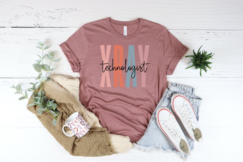 May include: A mauve t-shirt with the text "XRAY technologist" in black lettering. The letters are outlined in pink, orange, blue, and pink.