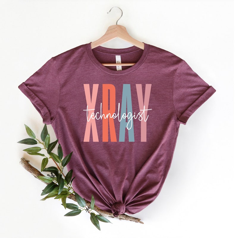 May include: A maroon t-shirt with the word "XRAY" in colorful letters and the text "technologist" in white script below.