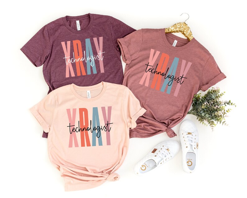 May include: Three t-shirts with the text "XRAY technologist" in colorful vertical stripes. The shirts are in different colors: maroon, pink, and light pink.