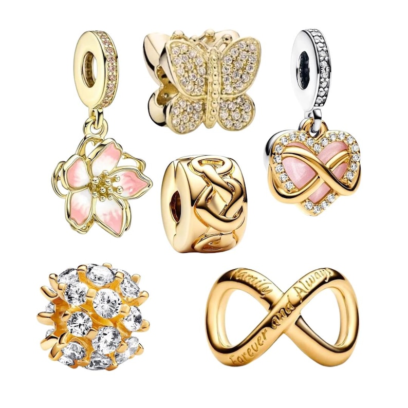 Puede incluir: Una colecci&oacute;n de abalorios y colgantes dorados. Los dise&ntilde;os incluyen una flor con esmalte rosa, una mariposa incrustada con piedras transparentes, un coraz&oacute;n infinito, un nudo celta, una esfera de piedras transparentes y un s&iacute;mbolo de infinito con texto.