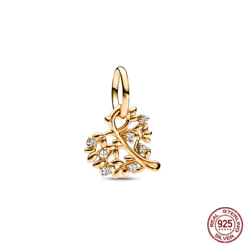 Puede incluir: Un charm dorado en forma de &aacute;rbol con hojas y peque&ntilde;as piedras transparentes. El charm est&aacute; dise&ntilde;ado para ser a&ntilde;adido a una pulsera o collar.