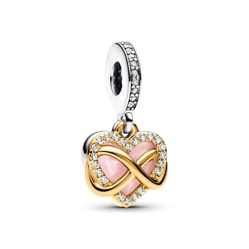 Puede incluir: Un charm en forma de coraz&oacute;n con un centro rosa y un dise&ntilde;o de s&iacute;mbolo de infinito dorado. El charm est&aacute; adornado con cristales transparentes y tiene una fianza plateada. Esta joya es un colgante.