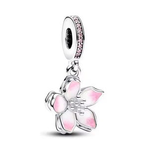 Puede incluir: Un charm de plata con un dise&ntilde;o floral. La flor tiene p&eacute;talos blancos con puntas rosas y un centro plateado. El lazo superior del charm est&aacute; adornado con piedras preciosas rosas. El charm cuelga de un lazo plateado.