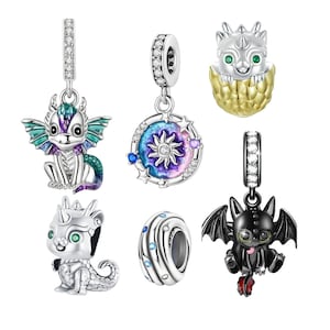 Puede incluir: Conjunto de siete abalorios de plata con diseños de dragón y celestiales. Los abalorios incluyen un dragón verde y morado, un dragón negro, un huevo de dragón dorado, un abalorio de sol y luna y un abalorio de espiral con detalles azules y blancos.