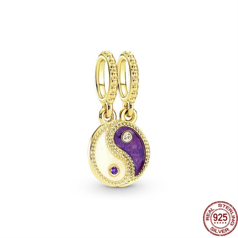 Puede incluir: Encanto dorado con un s&iacute;mbolo yin yang morado y blanco con dos peque&ntilde;as piedras transparentes. El encanto tiene dos lazos dorados para sujetarlo a una pulsera.
