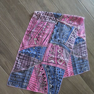 May include: A pink and blue patterned silk scarf with geometric designs. The scarf is folded in half and has a fringed edge.
