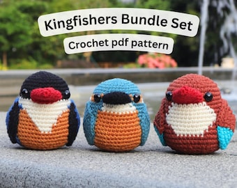 May include: Three crocheted kingfisher birds in a bundle set. The birds are in shades of blue, orange, brown, and black, with white bellies and red beaks. The text "Kingfishers Bundle Set" and "Crochet pdf pattern" are above the birds.