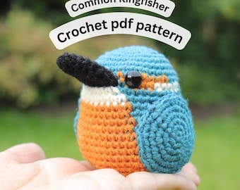 May include: A crocheted Common Kingfisher bird in shades of blue, orange, and black. The bird has a black beak and a black eye. The text "Common Kingfisher Crochet pdf pattern" is displayed above the bird.