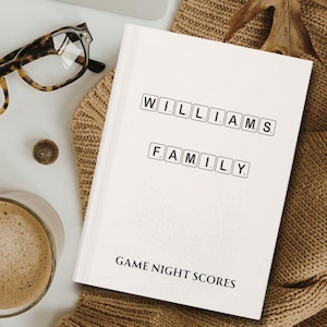 May include: White notebook with the words "WILLIAMS FAMILY GAME NIGHT SCORES" printed on the cover. The words are in a black font and are arranged in a block style, like Scrabble tiles.